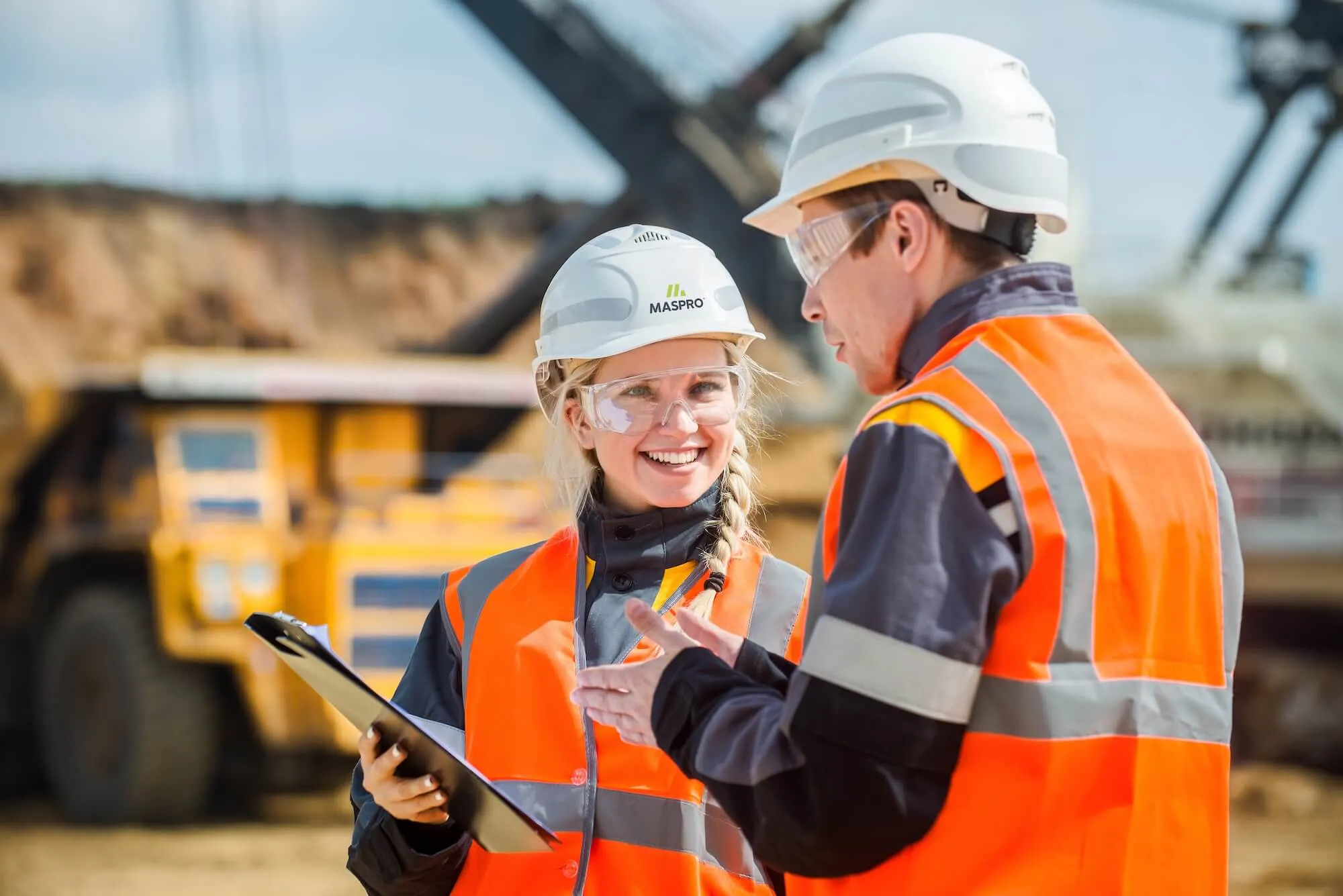 A women smiling and showing a clipboard to a man on a mine site