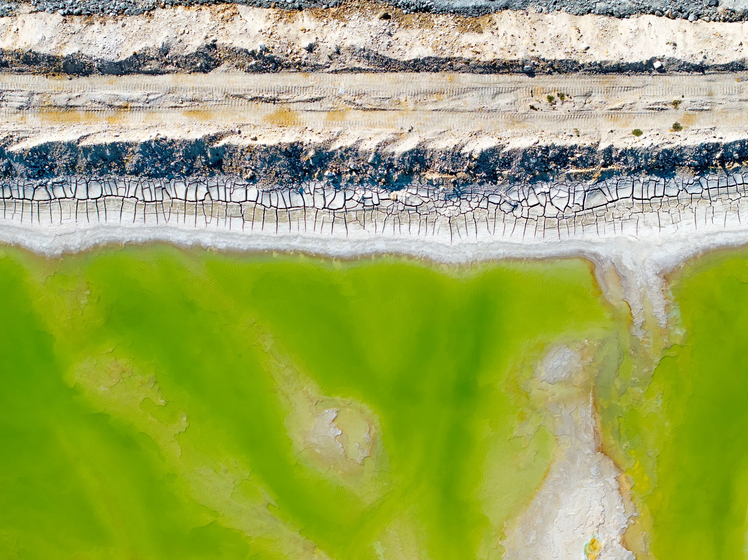Aerial view of treatment or oxidation pond with layered sediment patterns and geometric water containment structures.