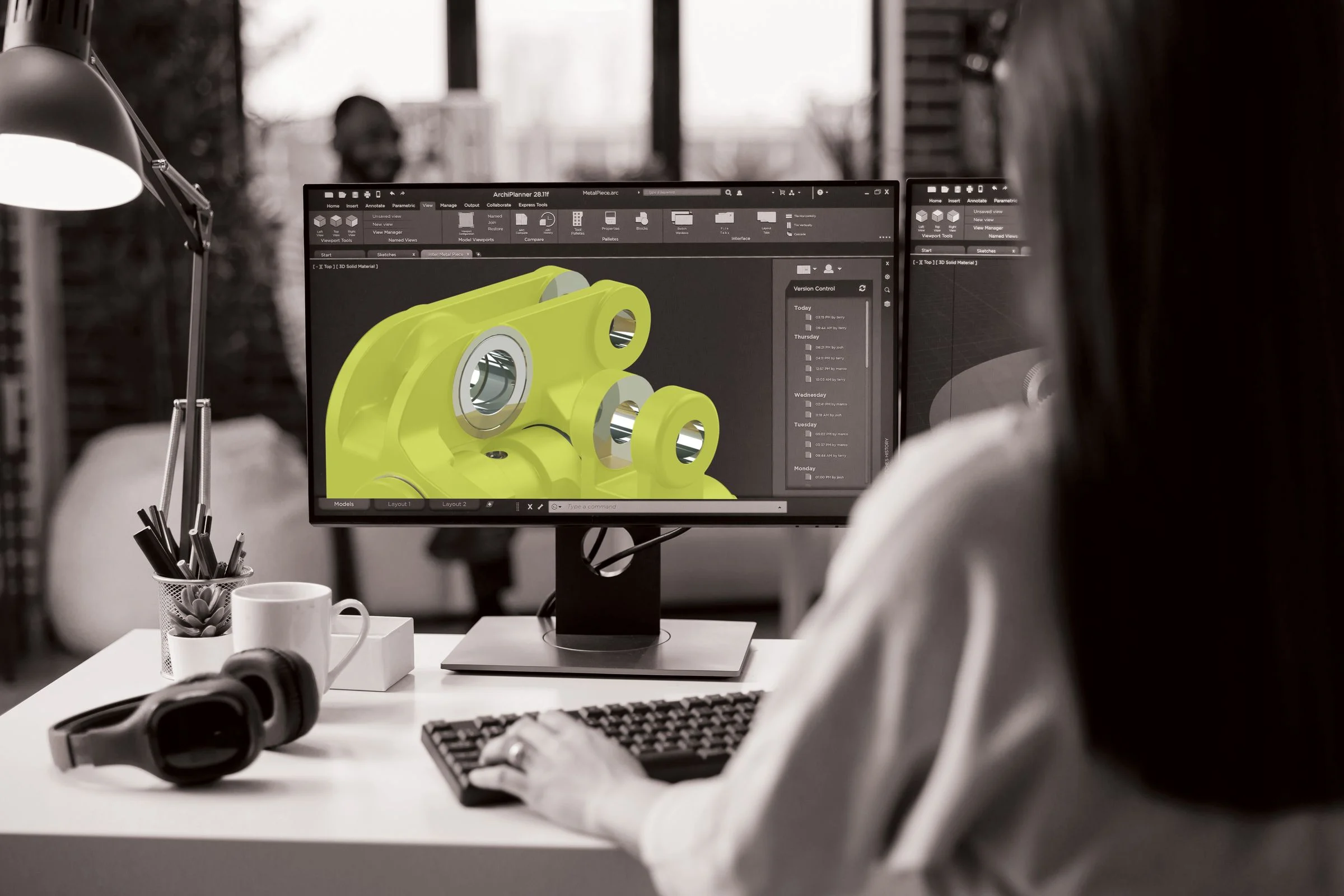 Engineer viewing CAD model of a yellow cradle assembly in Autodesk on office monitor.