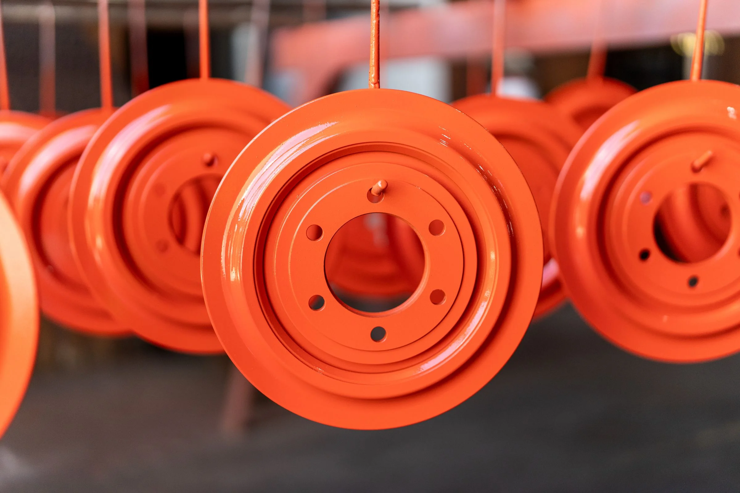 Close-up of bright orange injection-molded or machined pulley components or wheel assemblies hanging from cables.